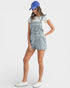 Person wearing a denim overall dress, white sneakers, and a blue cap on a white background