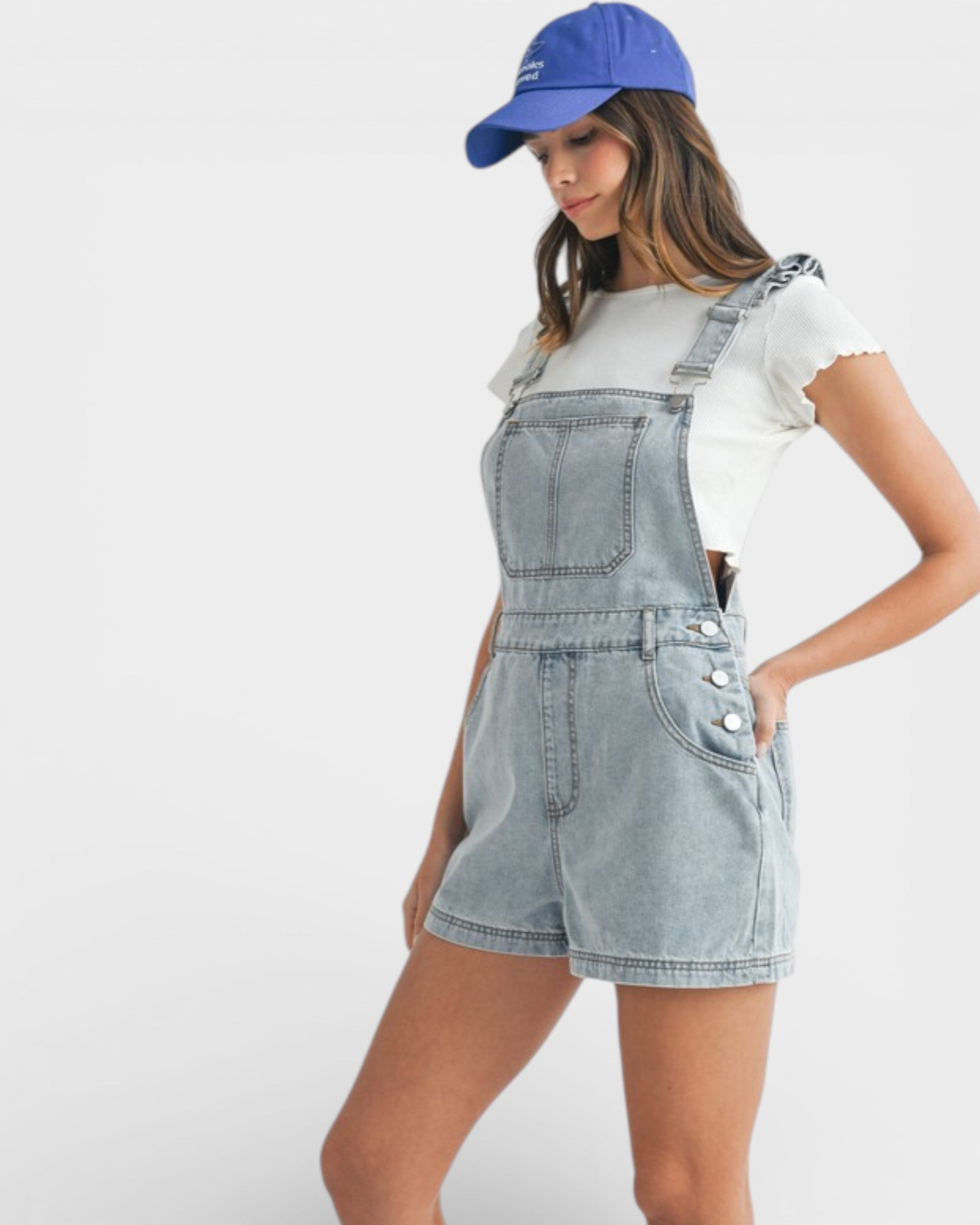 Woman wearing denim overalls and a blue cap on a white background
