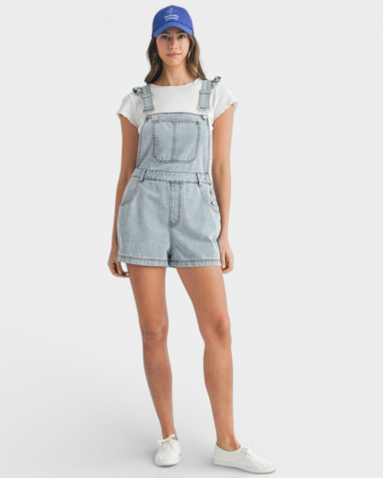 Woman wearing denim overalls and a blue cap on a white background