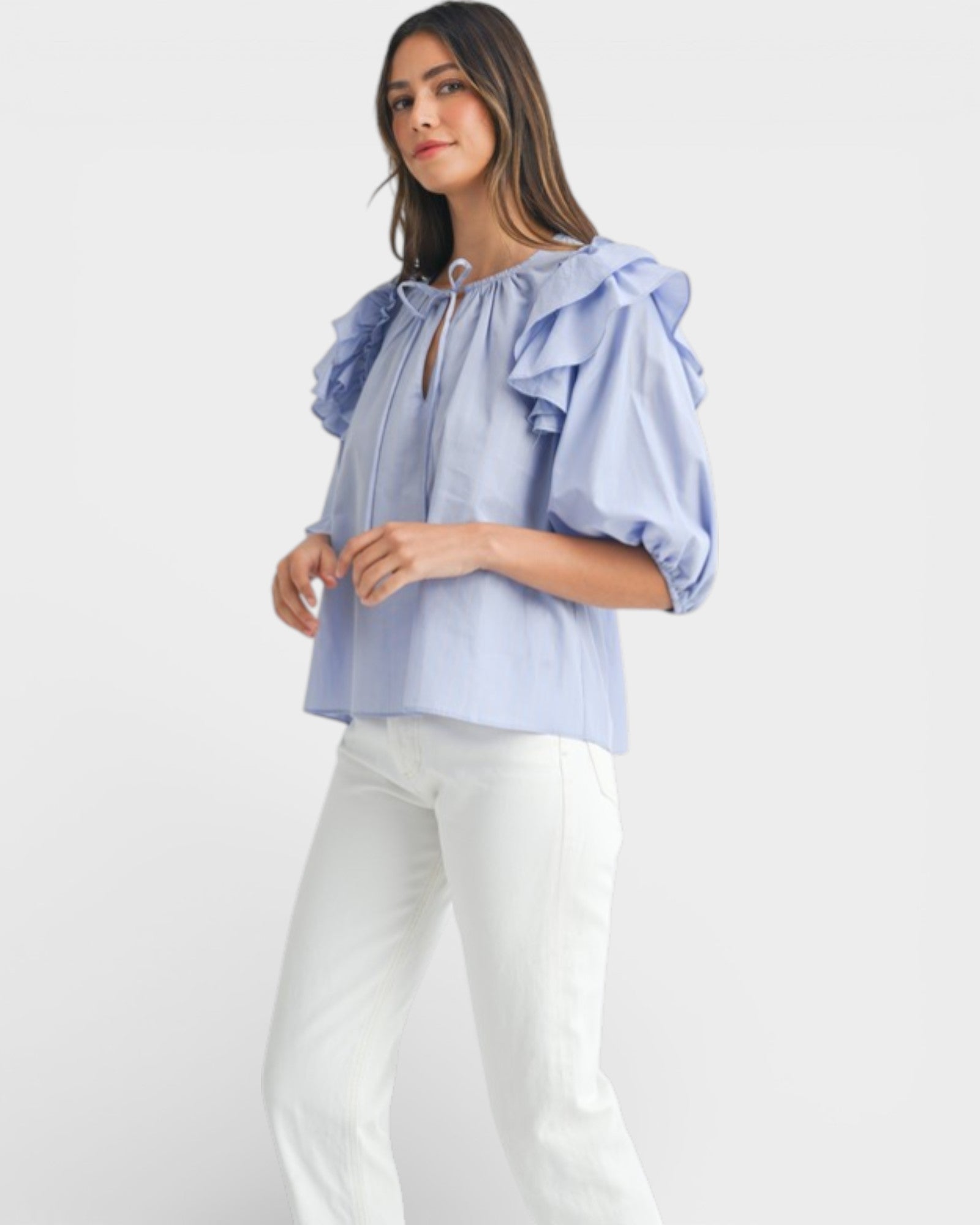 Woman wearing a light blue blouse with ruffled shoulders on a white background