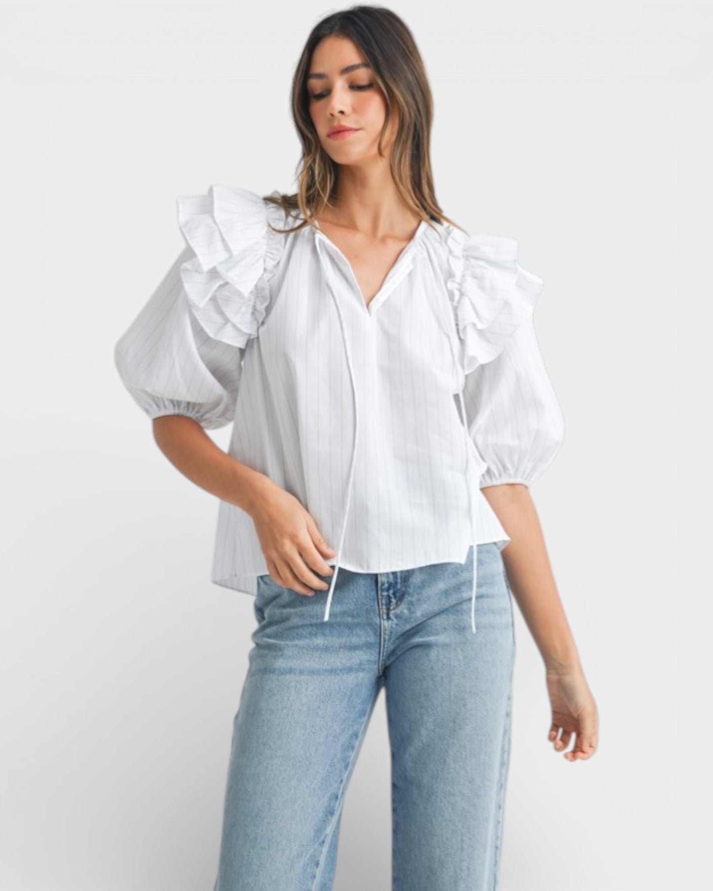 Woman wearing a white blouse with ruffled sleeves and light blue jeans on a white background