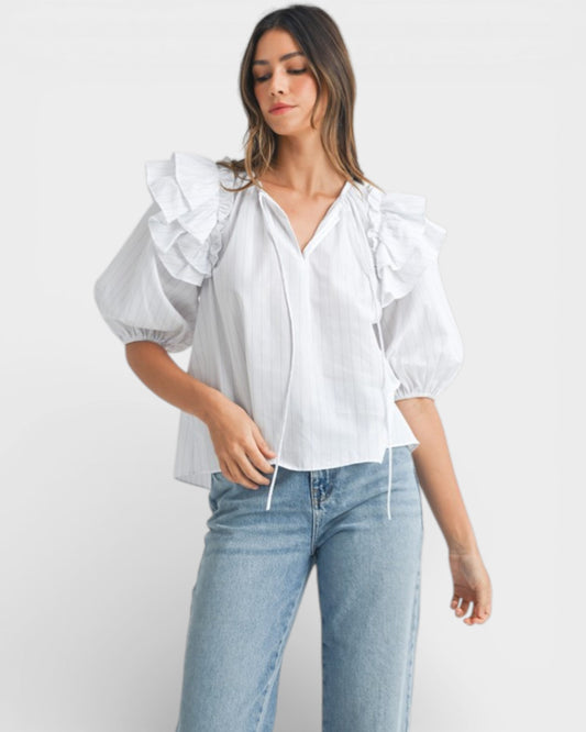 Woman wearing a white blouse with ruffled sleeves and light blue jeans on a white background