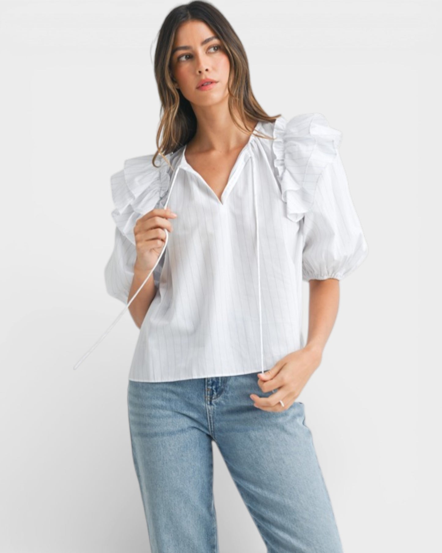 Woman wearing a white blouse with puff sleeves and blue jeans on a white background