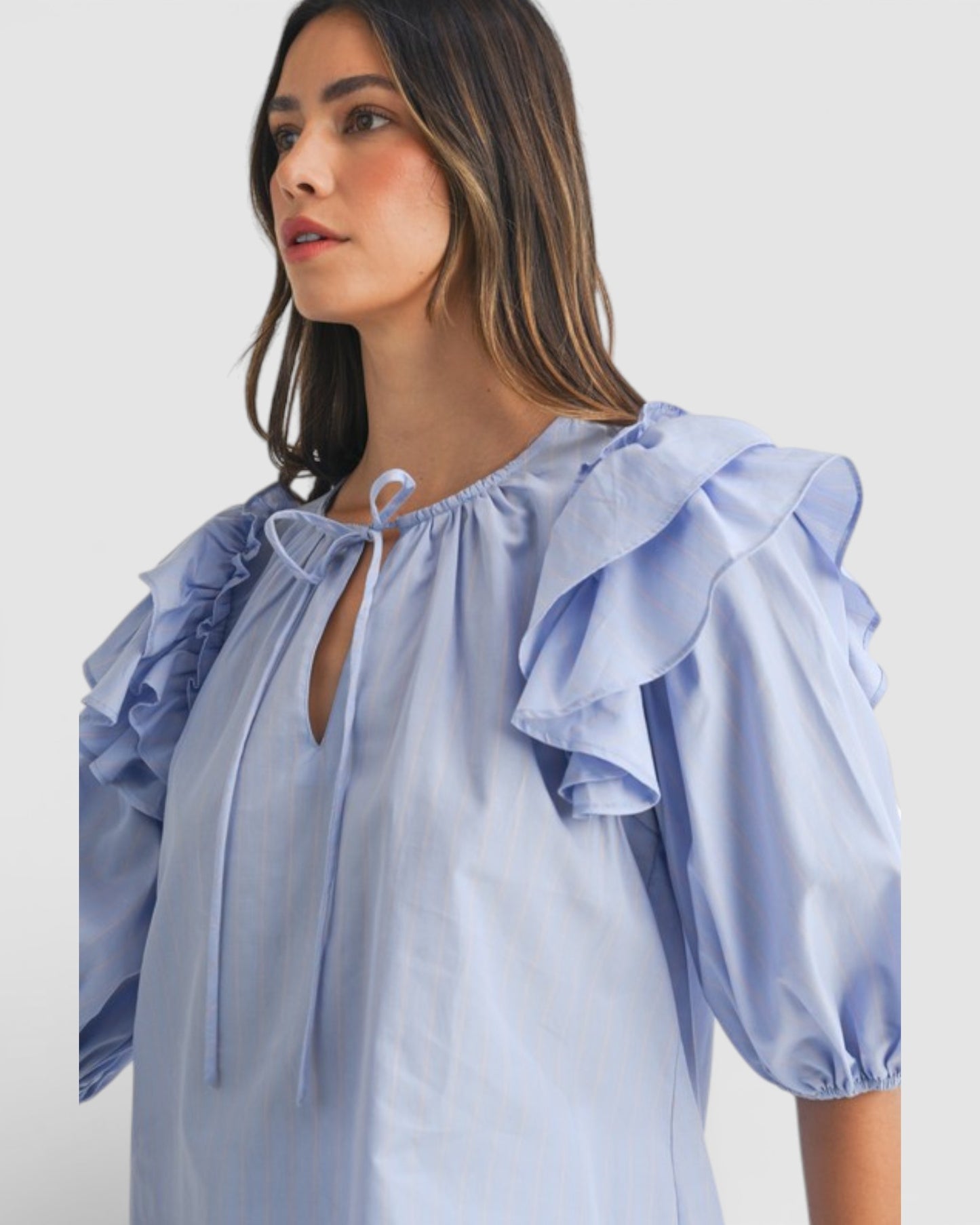 Woman wearing a light blue blouse with ruffled sleeves on a plain background