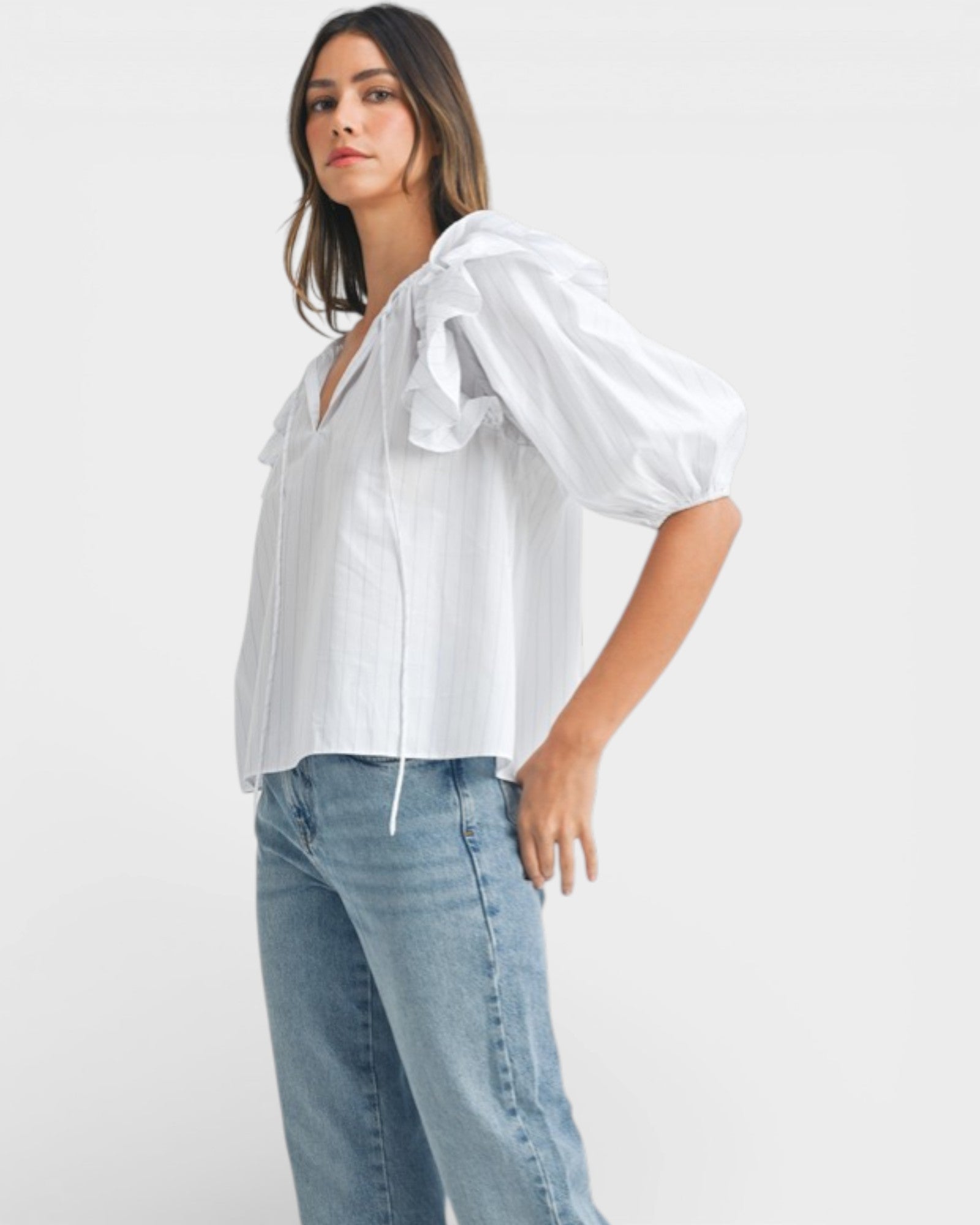 Woman wearing a white blouse and light blue jeans on a plain background