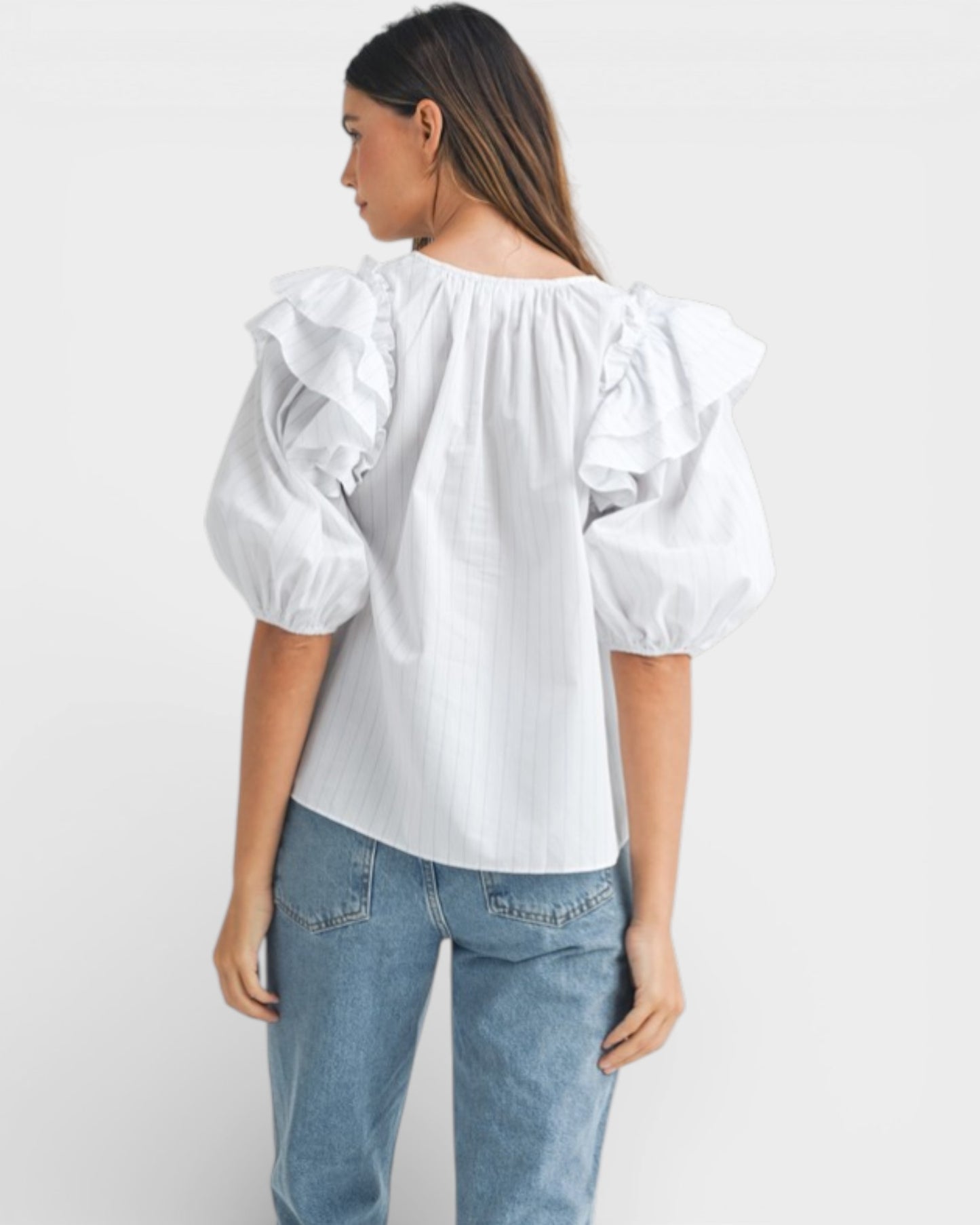 Woman wearing a white blouse with ruffled sleeves and light blue jeans on a white background