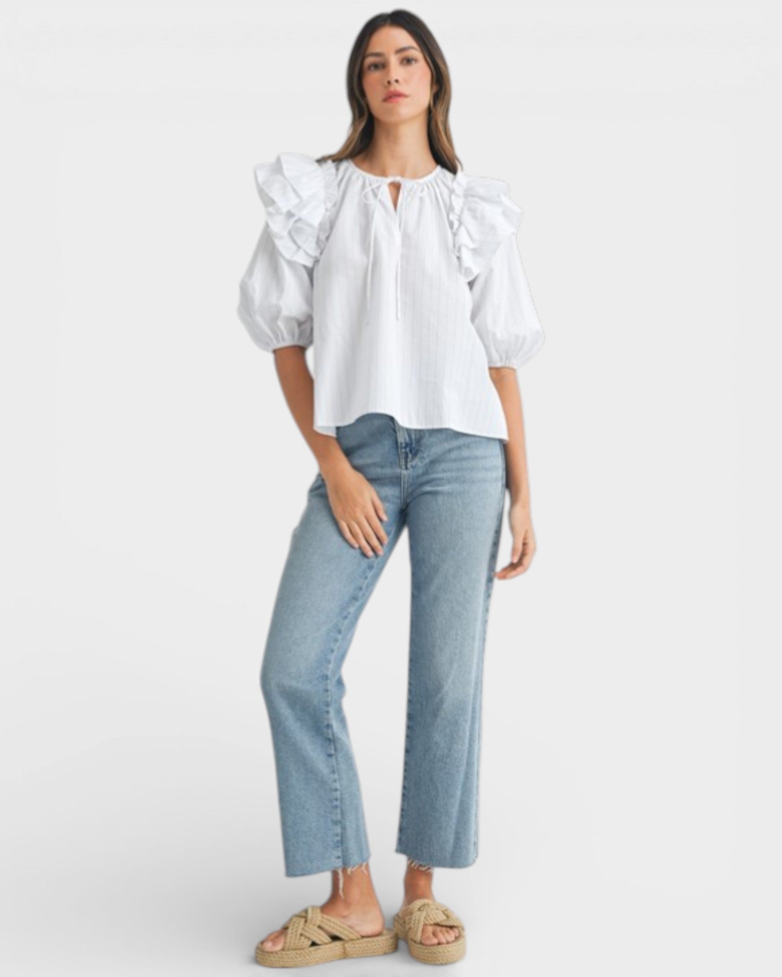 Woman wearing a white blouse with ruffled sleeves and light blue jeans on a white background