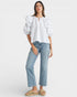 Woman wearing a white blouse with ruffled sleeves and light blue jeans on a white background