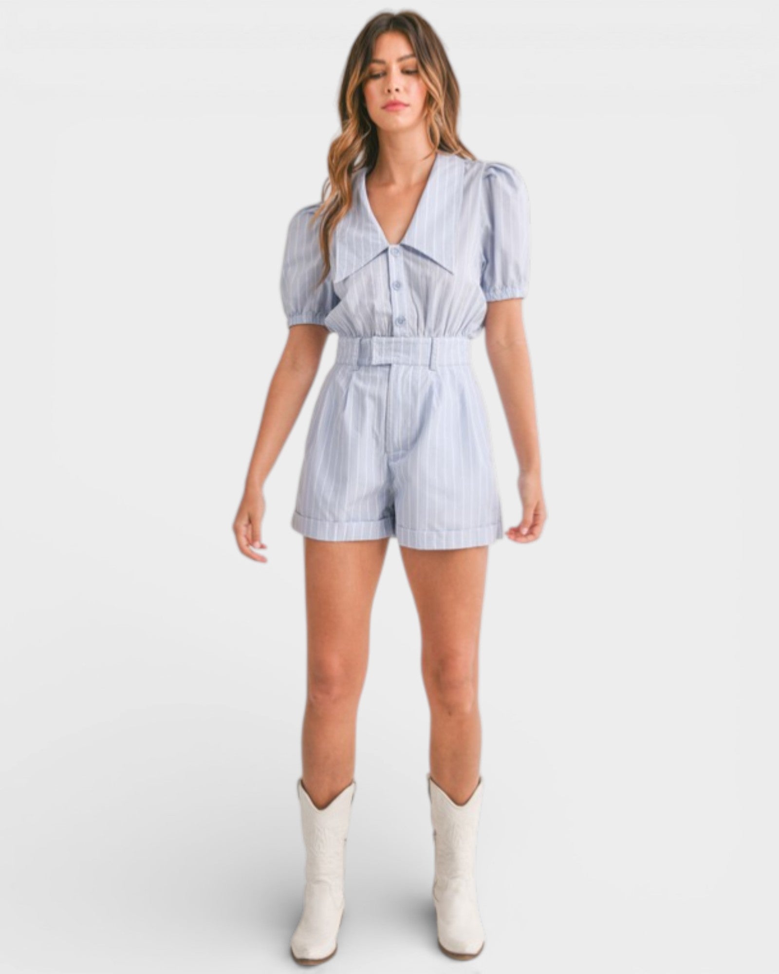 Woman wearing a light blue striped romper with white boots on a white background