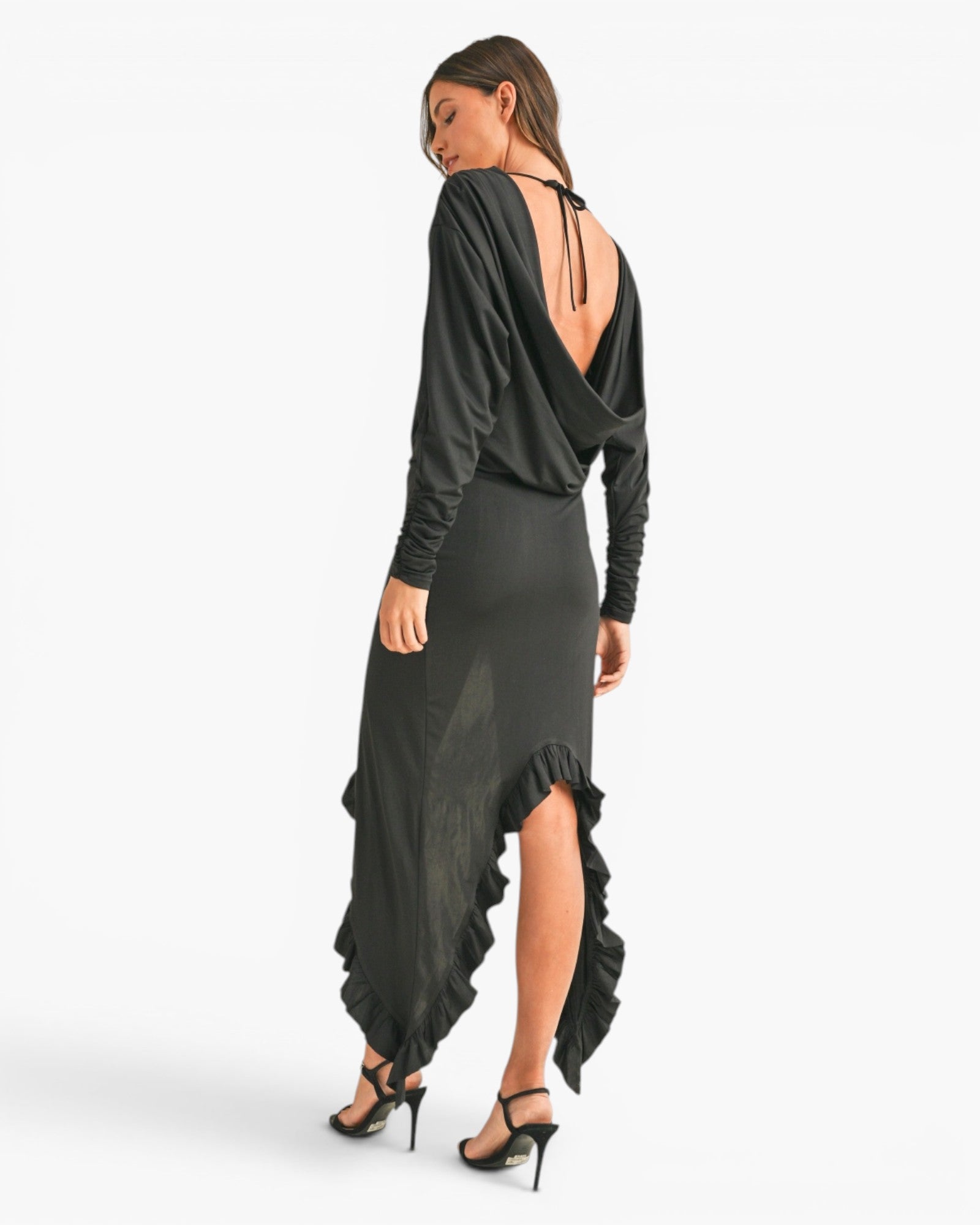 A woman modeling a black long-sleeve maxi dress with a draped open back, shown from the rear against a clean white studio background.