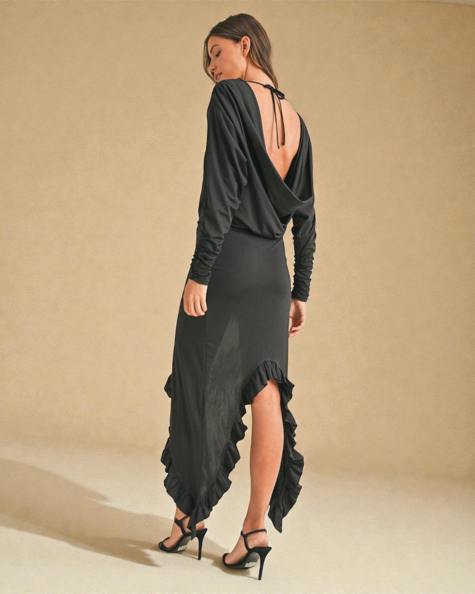 Woman wearing a dark gray dress with long sleeves and a slit skirt on a beige background