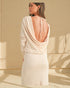 Woman wearing a beige dress with an open back in a sunlit room.