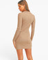 A woman wearing a beige ribbed long-sleeve mini dress, shown from a side-back angle against a plain white studio background.