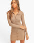 A woman modeling a beige ribbed long-sleeve button-front mini dress against a plain light gray studio background.