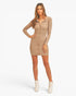 A woman modeling a beige ribbed long-sleeve mini dress with a button-front collar, paired with white ankle boots, against a plain white studio background.