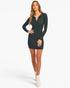 A woman modeling a black long-sleeve mini button-front dress with a collared neckline, paired with white ankle boots, against a plain light gray studio background.