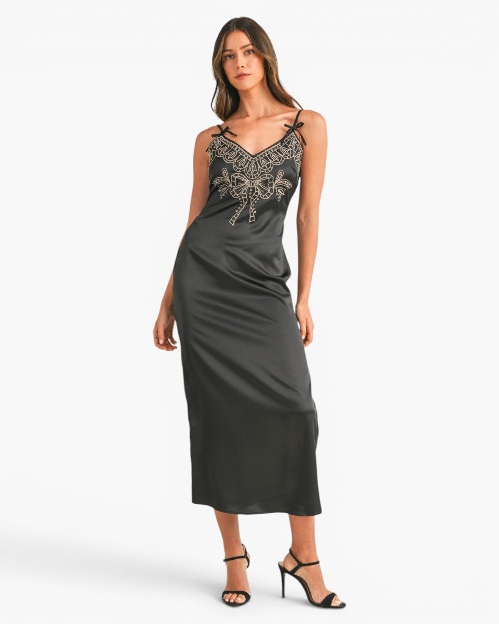 A woman modeling a dark gray satin midi slip dress with silver beaded embroidery on the bodice, paired with black strappy high-heeled sandals, against a plain white studio background.