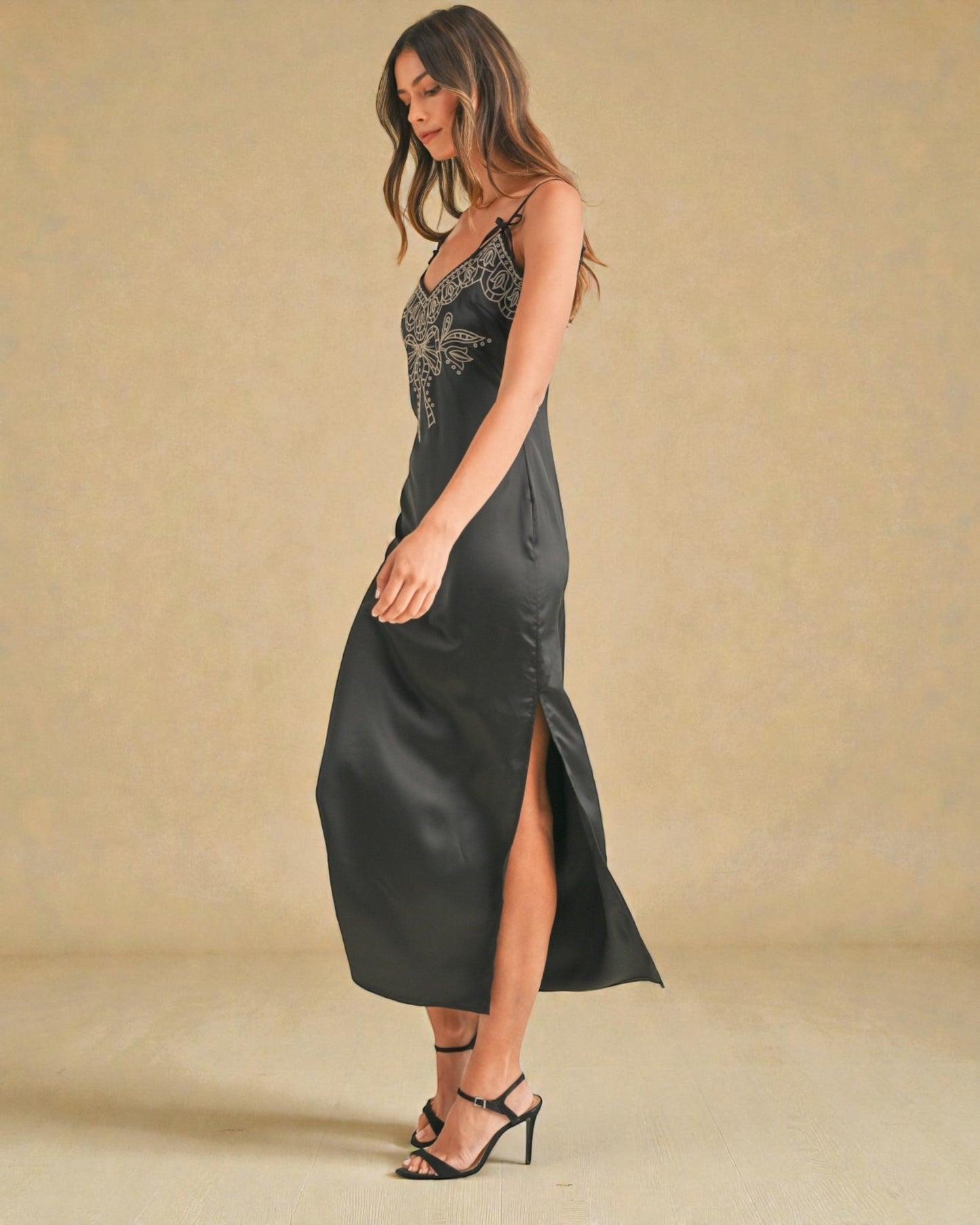 Woman wearing a black slip dress with embroidery on a beige background