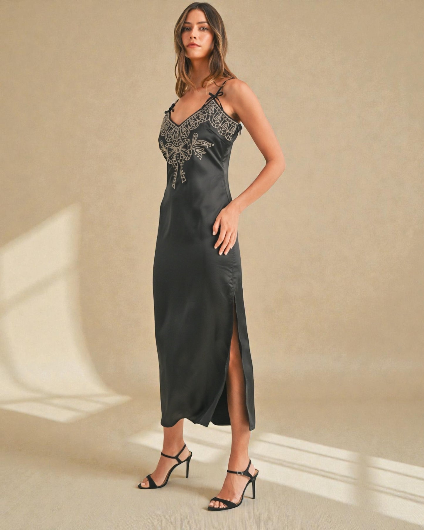 Woman wearing a black satin slip dress with lace detailing on a beige background