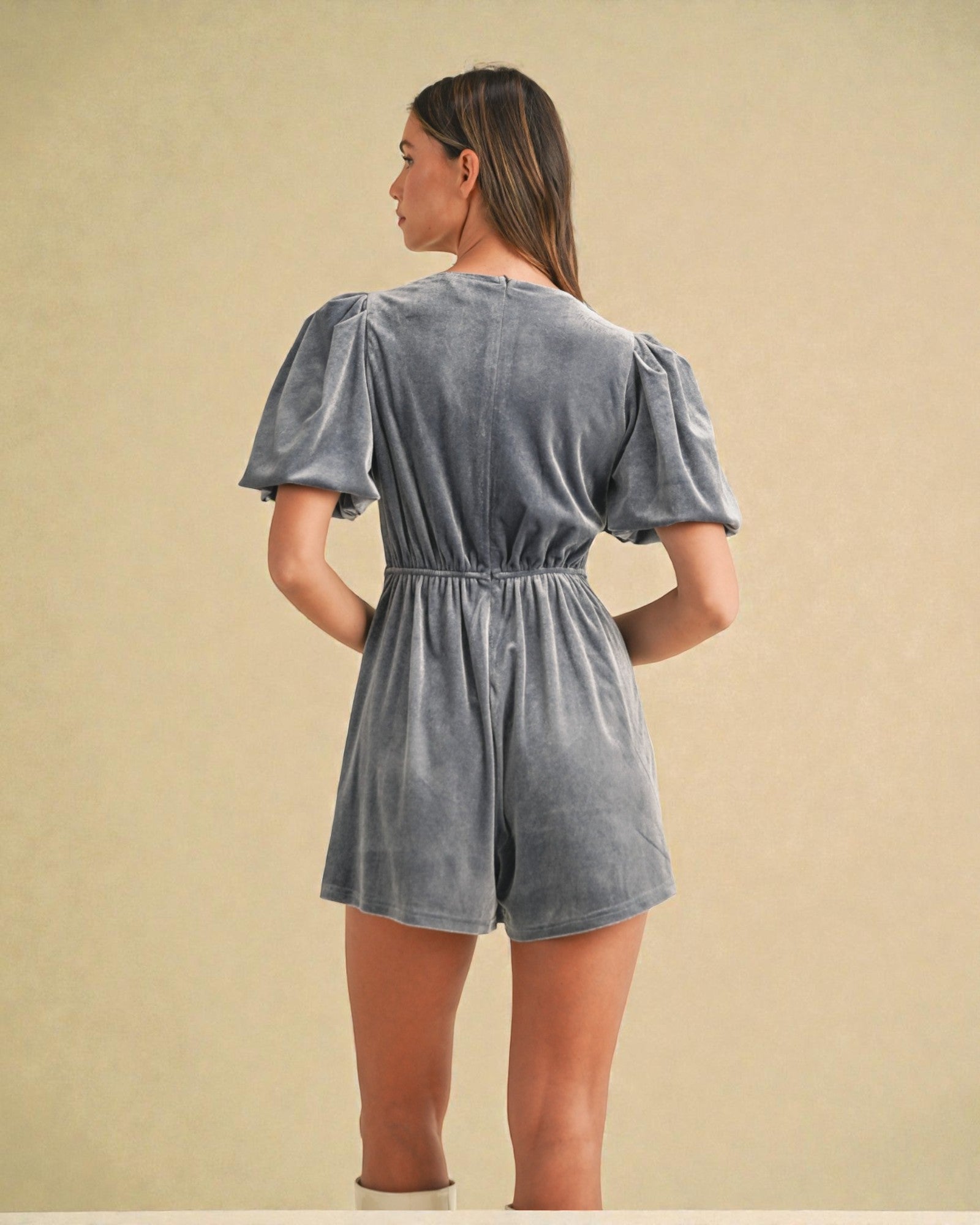 Woman wearing a gray romper against a beige background