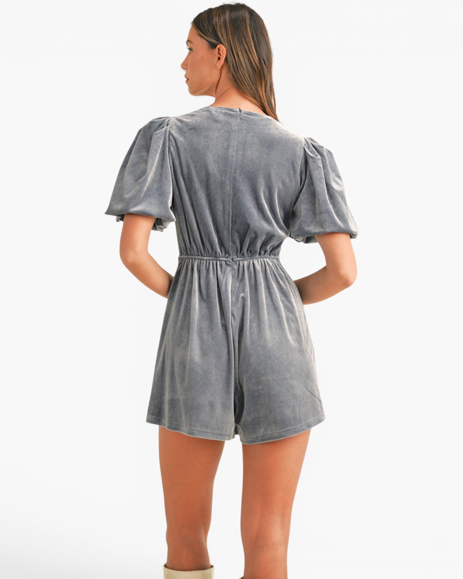 A woman shown from the back wearing a gray velvet short romper with puff sleeves and an elastic waist, photographed against a plain white studio background.