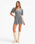 A woman modeling a gray velvet romper with puff sleeves, a V-neckline, and three decorative bow details on the front, paired with cream-colored knee-high boots against a plain white background.