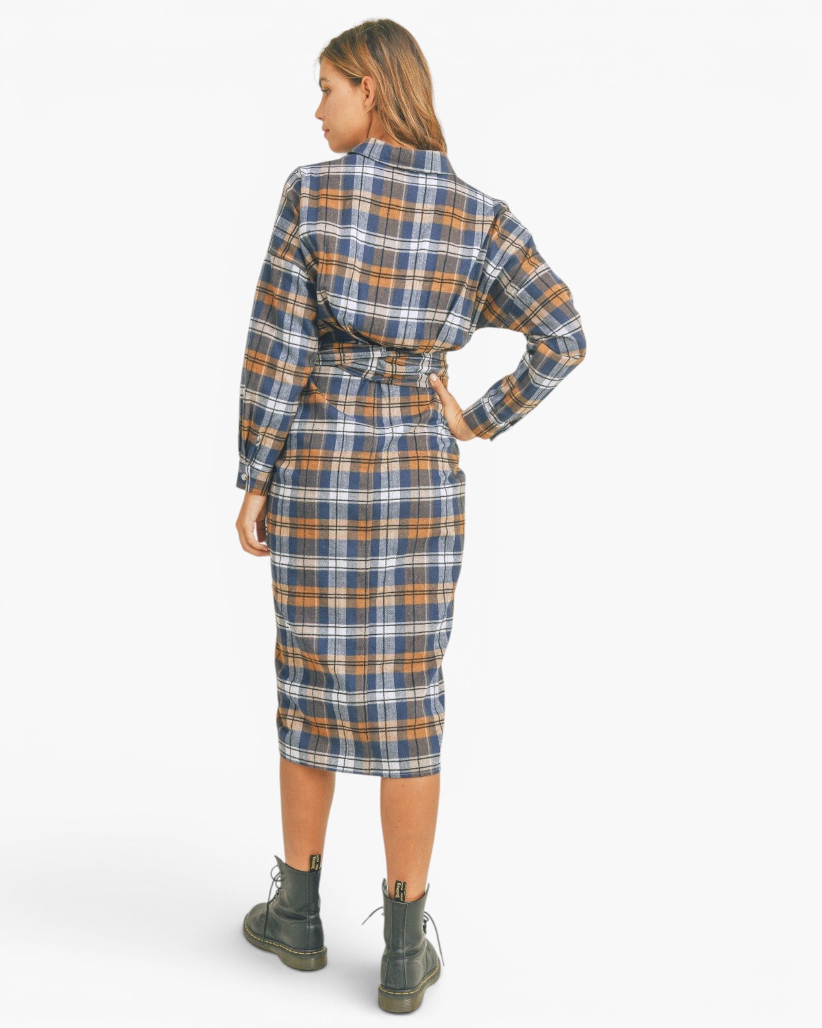 A woman shown from the back wearing a long-sleeve plaid shirt dress with a matching tie belt, paired with dark combat boots, against a plain white studio background.