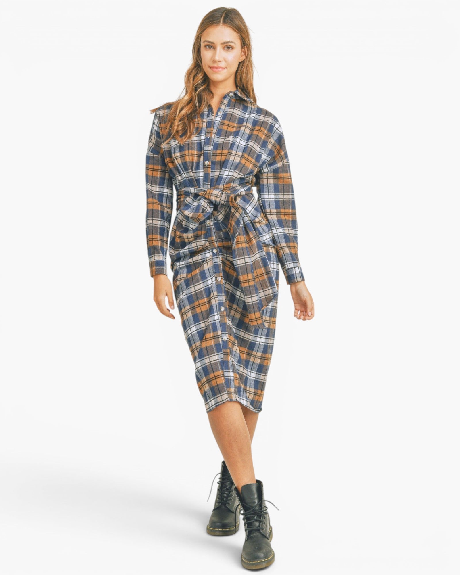 A woman modeling a long-sleeve plaid shirt dress with a matching tie belt, paired with black lace-up boots, against a plain white studio background.