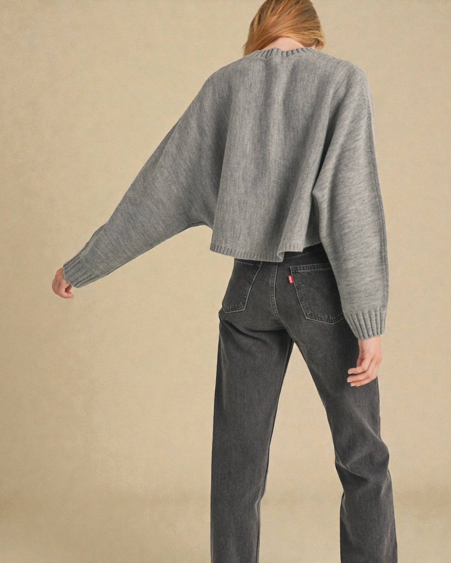 Person wearing a gray sweater and dark jeans against a beige background