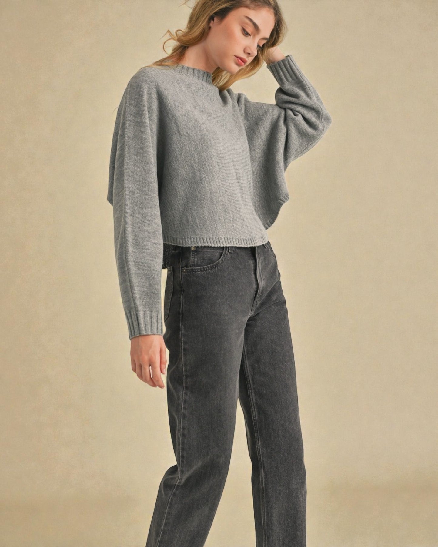 Woman wearing a gray sweater and dark jeans against a beige background