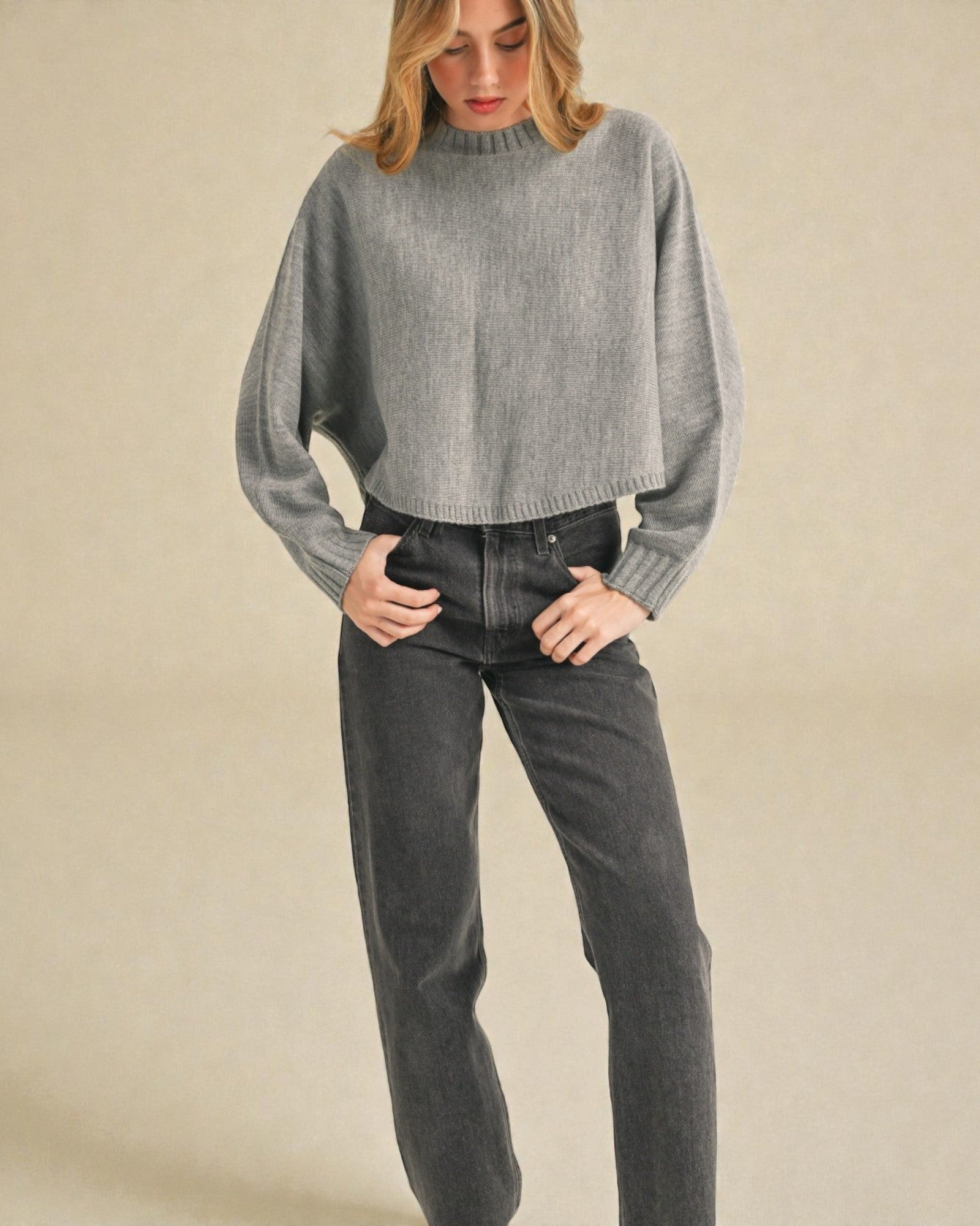 Woman wearing a gray sweater and black pants against a beige background