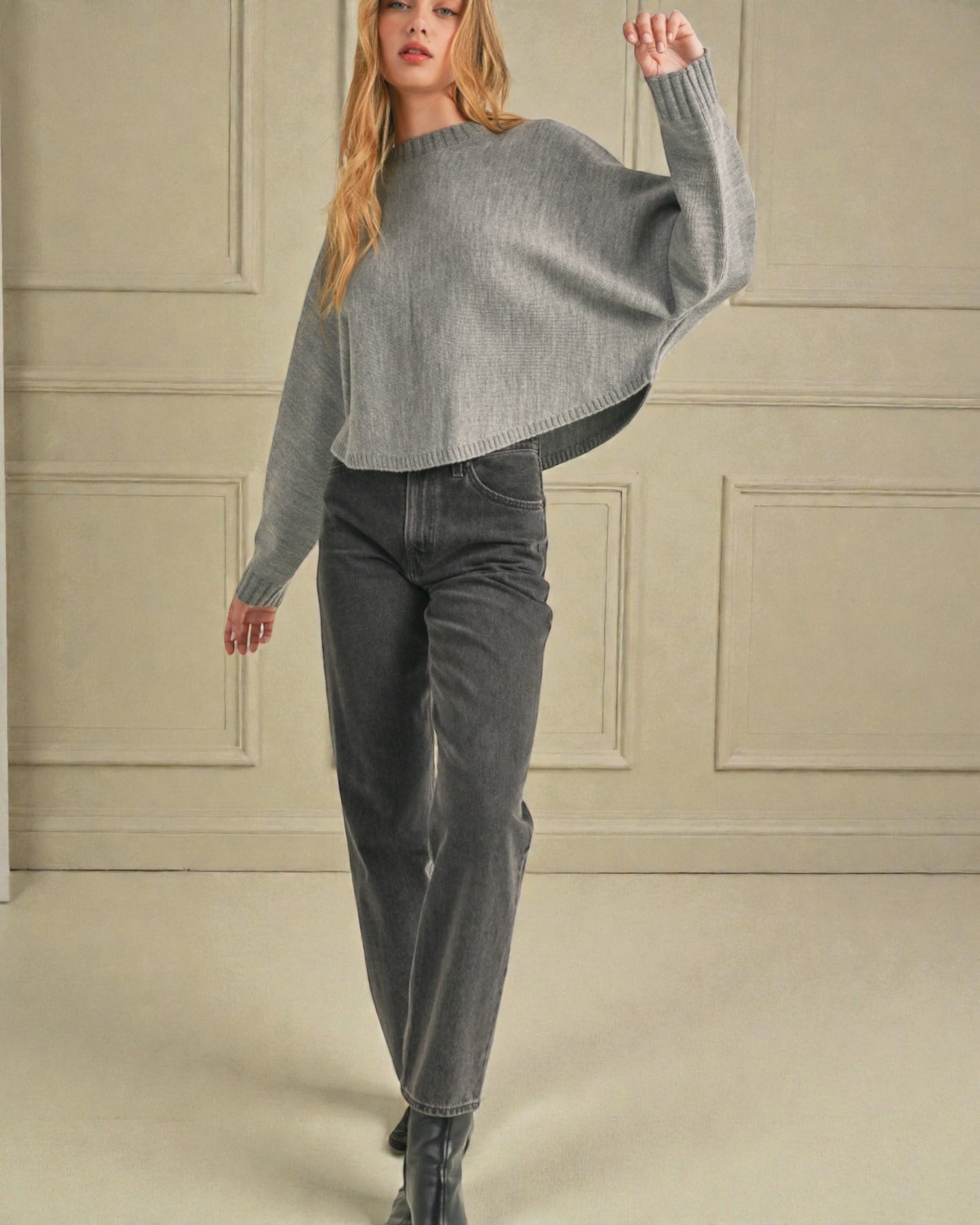 Woman wearing a gray sweater and jeans in a neutral setting