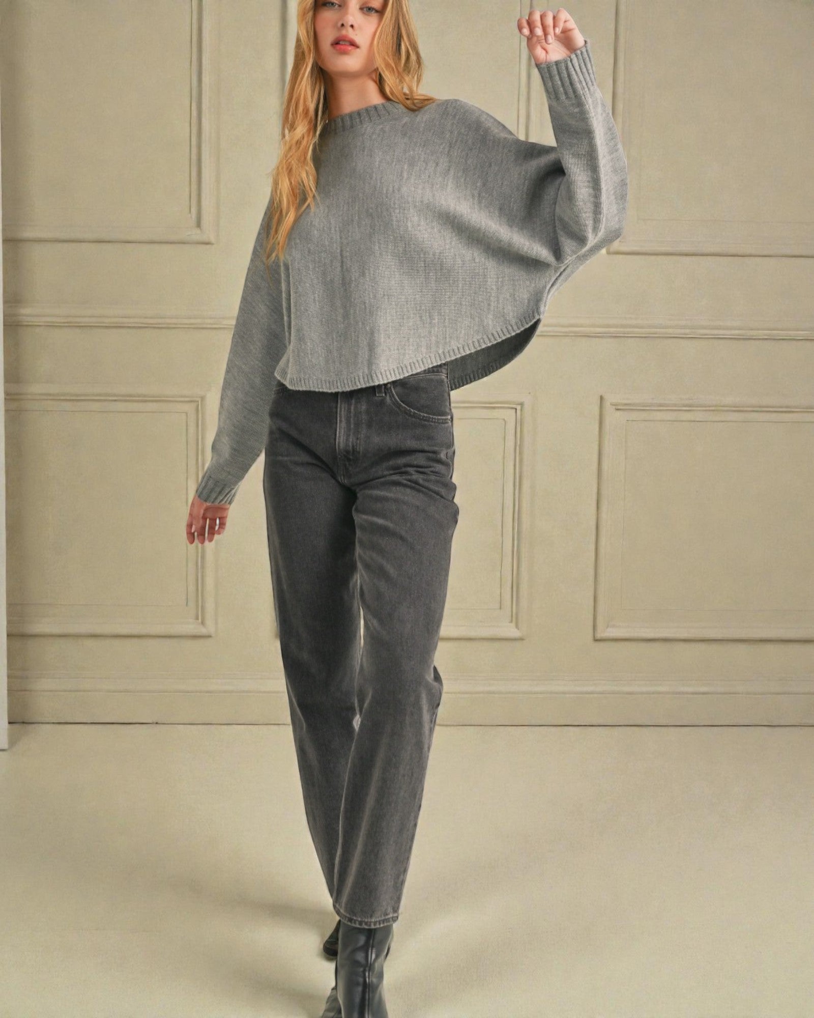 Woman wearing a gray sweater and jeans in a neutral setting