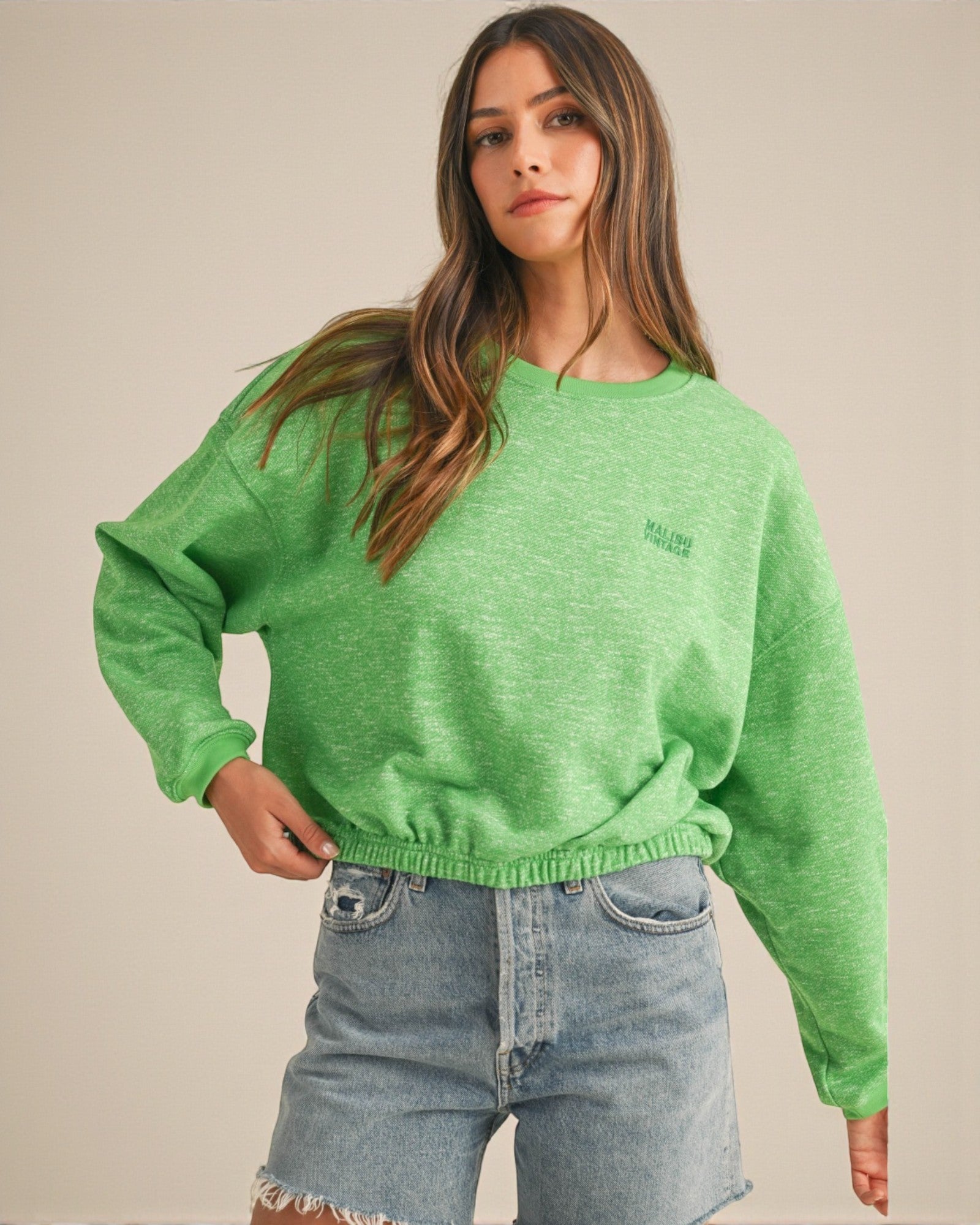 Woman wearing a green sweatshirt with a brand logo on a beige background
