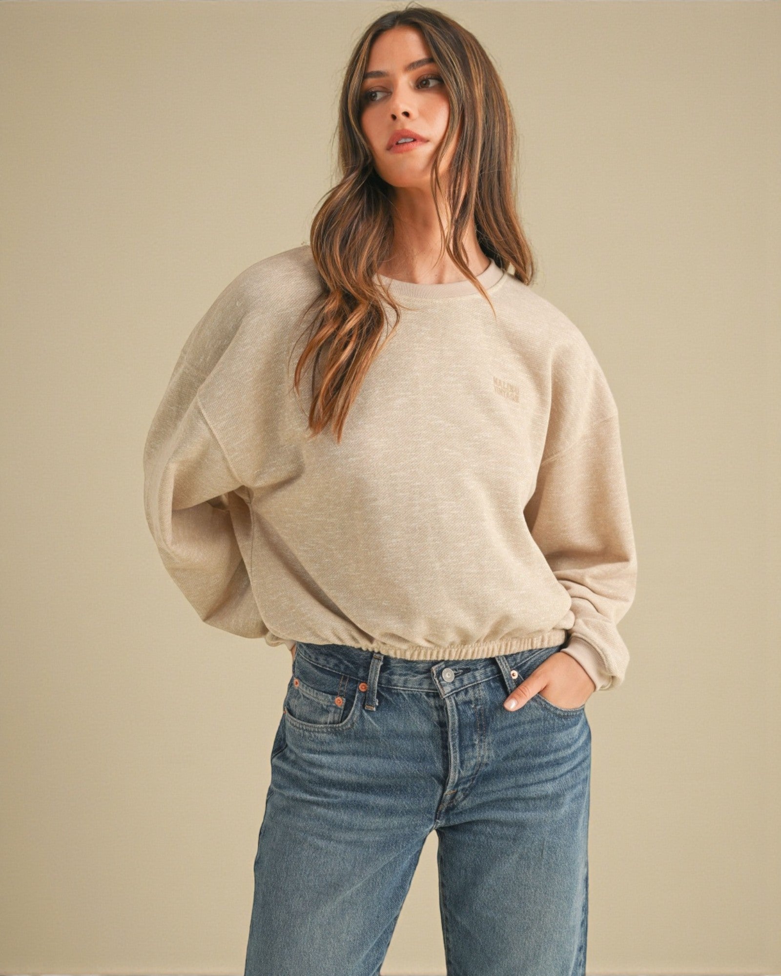 Woman wearing a beige sweater and blue jeans against a beige background