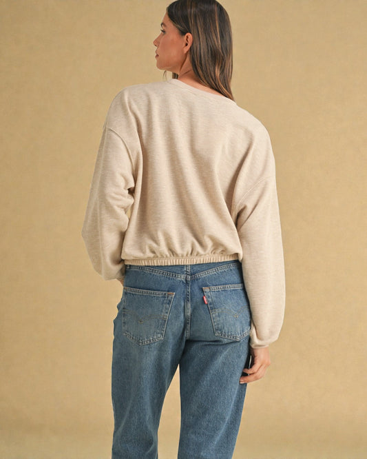 Person wearing a beige sweater and blue jeans against a beige background