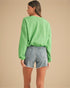 Person wearing a green sweater and denim shorts on a beige background