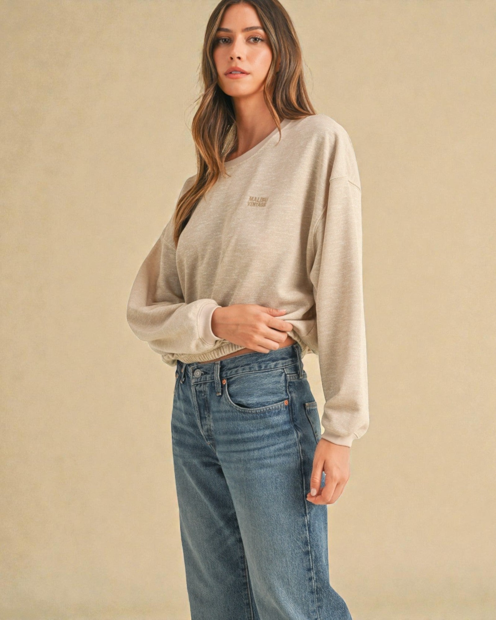 Woman wearing a light gray sweater and blue jeans against a beige background
