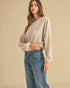 Woman wearing a light gray sweater and blue jeans against a beige background