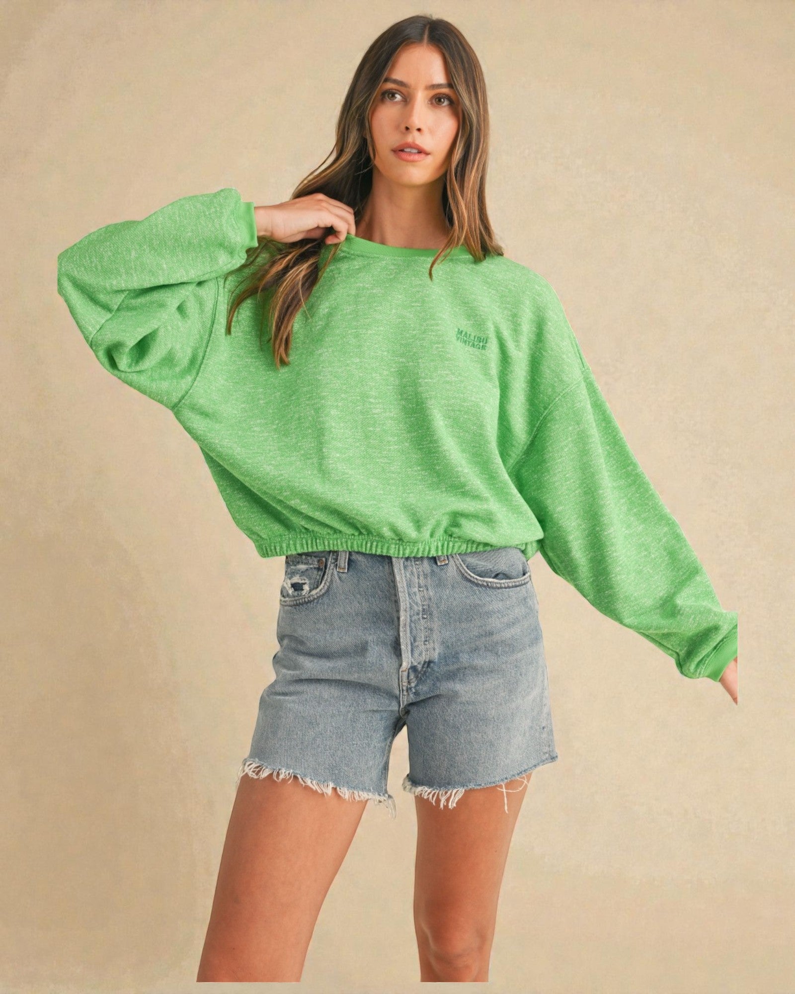 Woman wearing a green sweater and denim shorts on a beige background