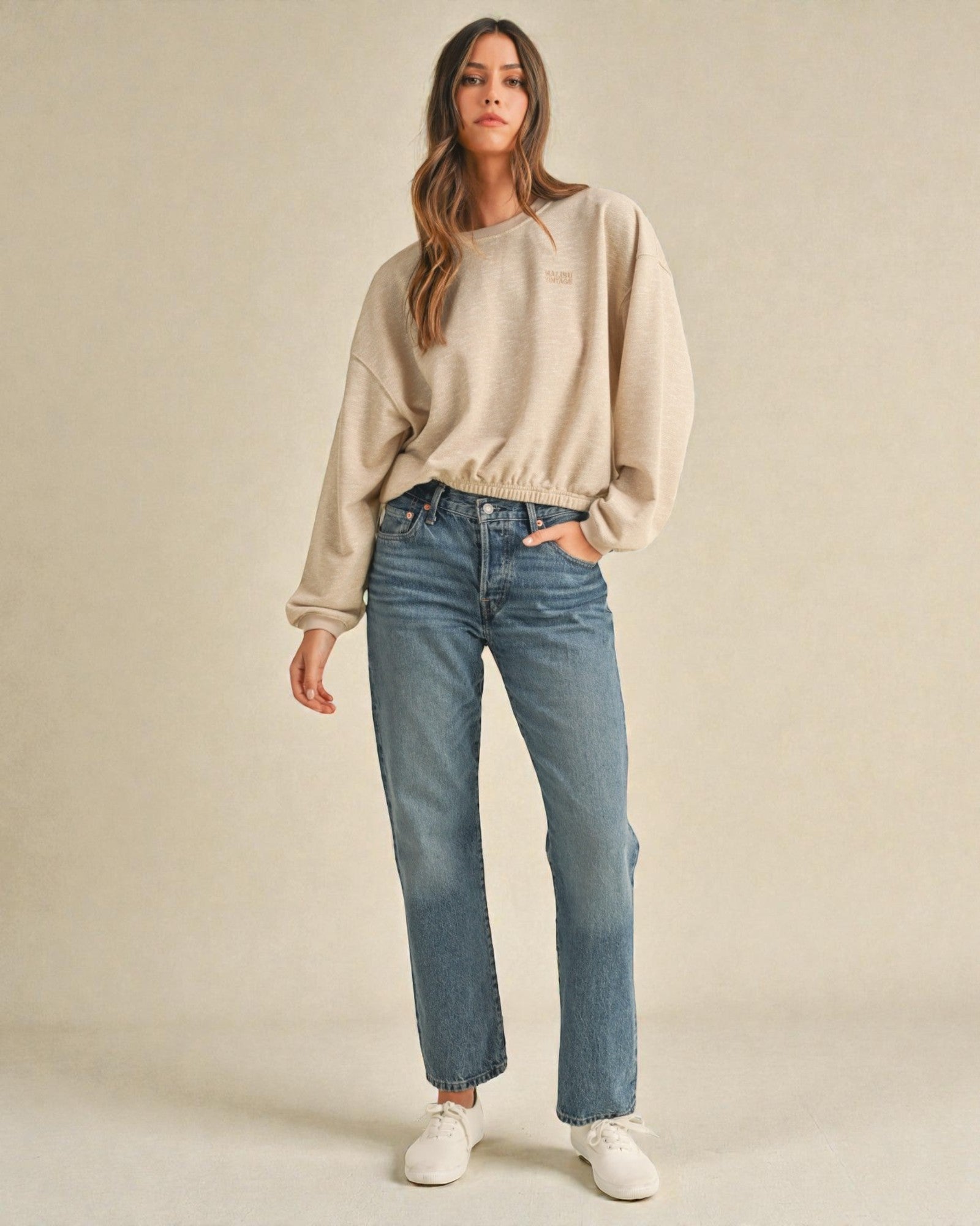 Woman wearing a beige sweater and blue jeans against a plain background