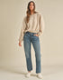 Woman wearing a beige sweater and blue jeans against a plain background