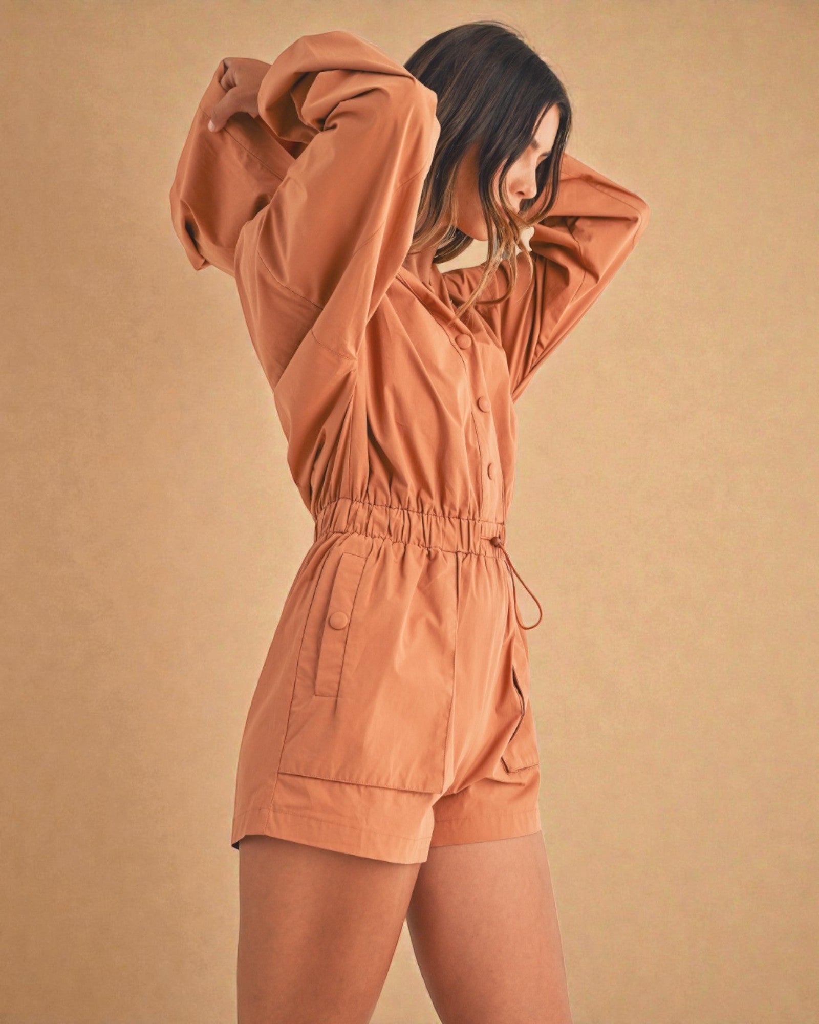 Person wearing a brown romper against a beige background