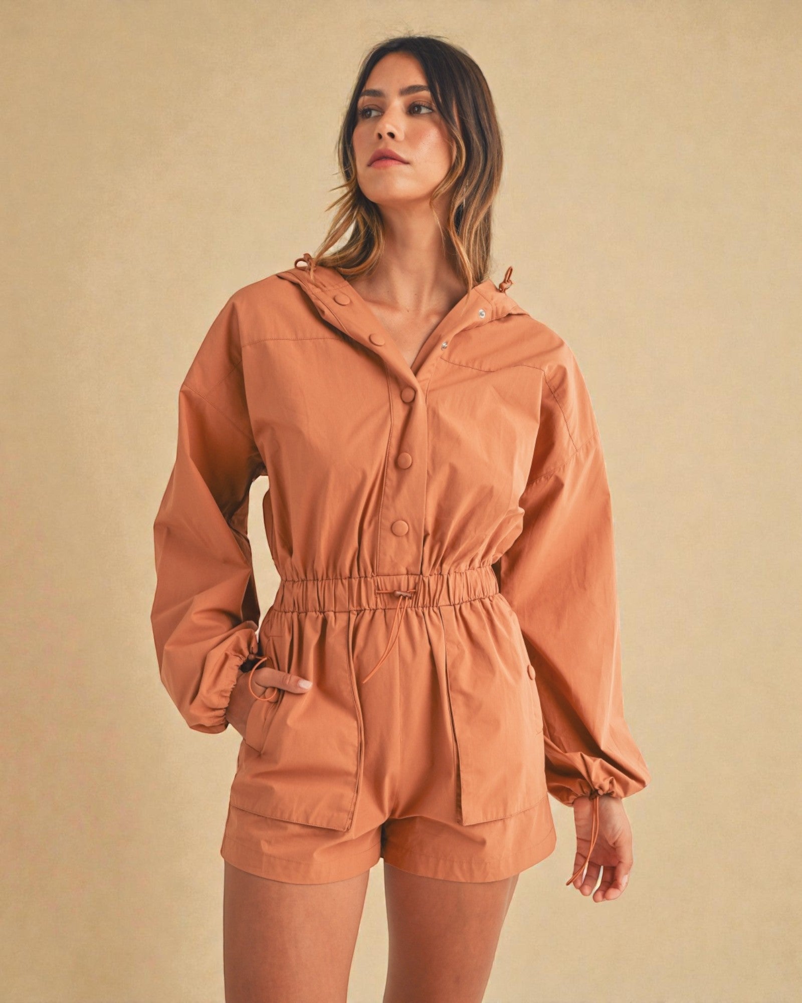 Woman wearing a brown jacket and shorts set against a beige background