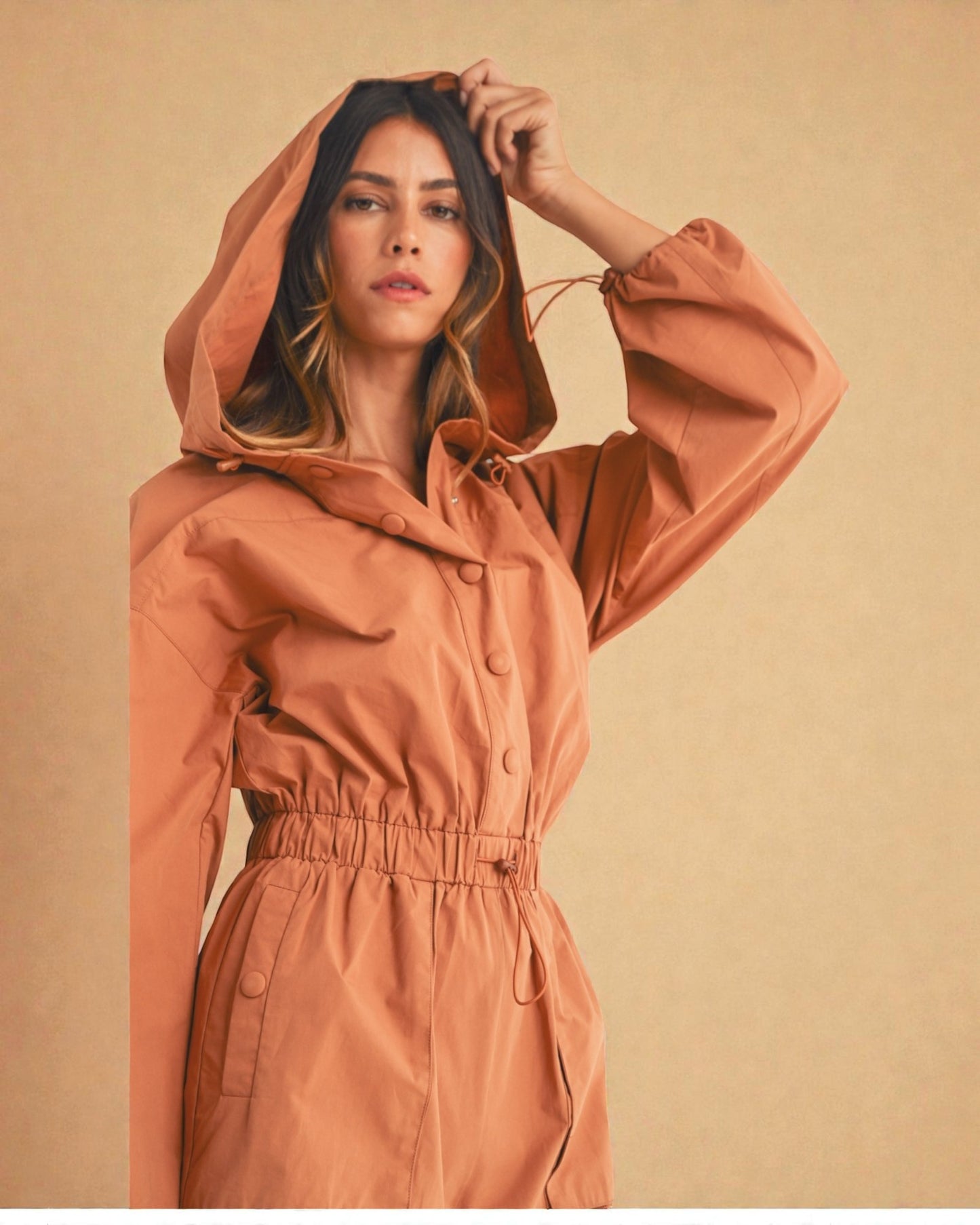 Woman wearing a brown hooded coat against a beige background