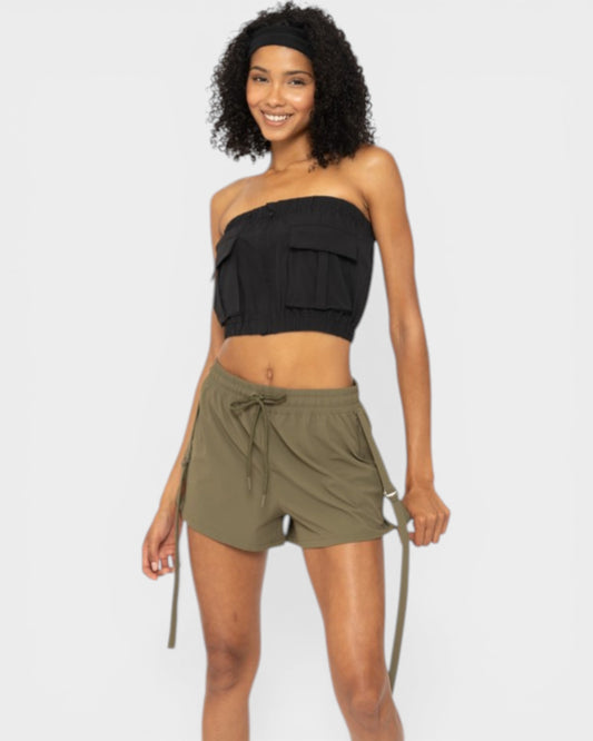 Woman wearing a black strapless top and olive green shorts on a white background