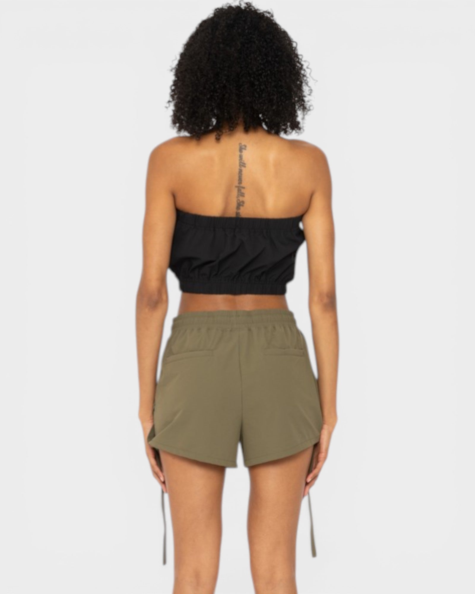 Person wearing a black strapless top and olive green shorts on a white background