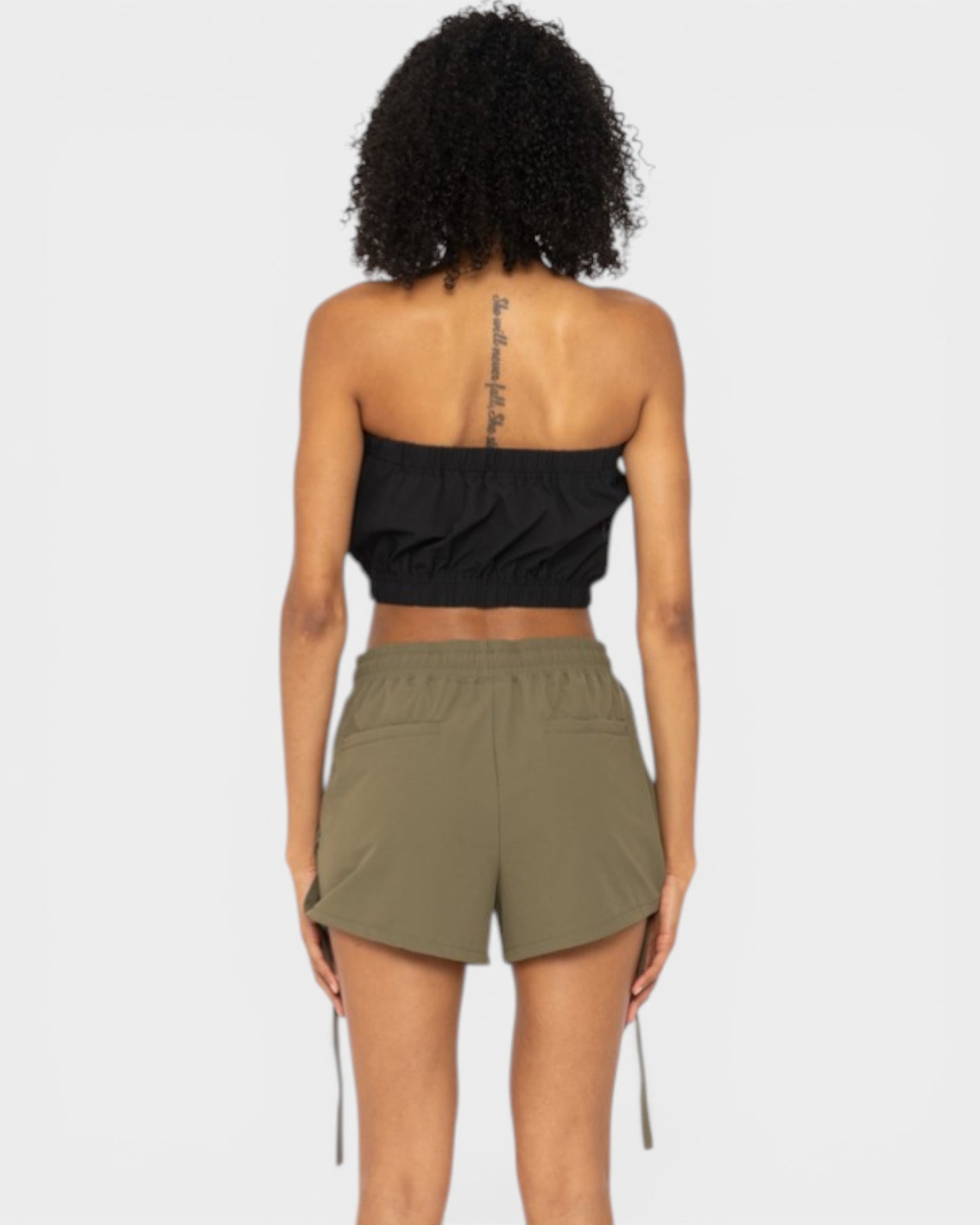 Person wearing a black strapless top and olive green shorts on a white background