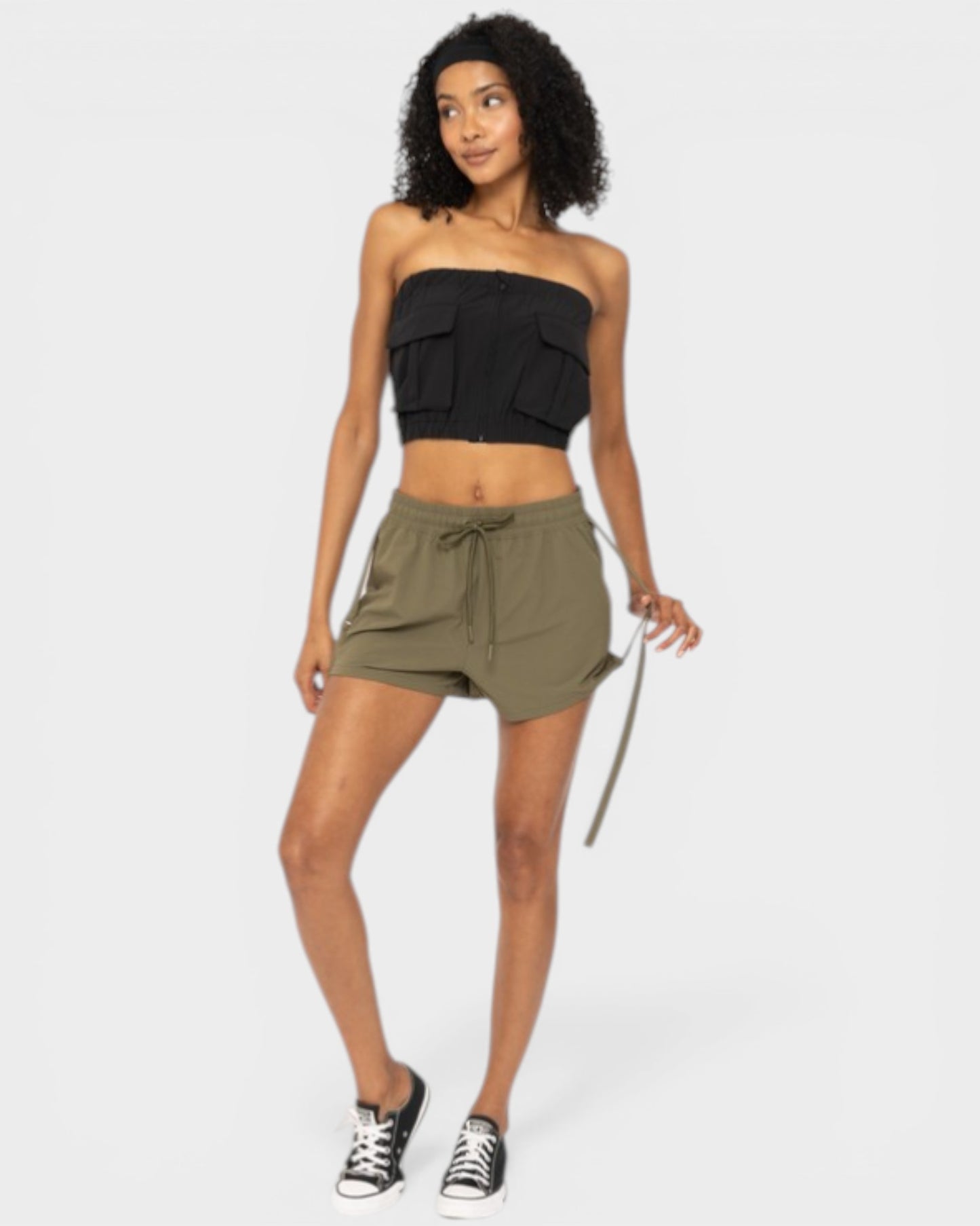 Woman wearing a black strapless top and olive green shorts on a white background