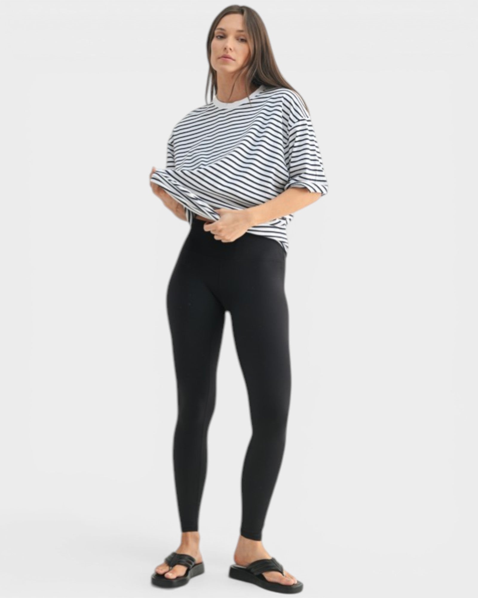 Woman wearing a black and white striped shirt and black leggings on a white background